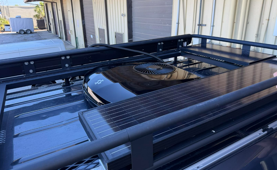 OutEquip black edition 12V rooftop AC installed on travel trailer roof beside solar panels, low 6.3-inch profile visible